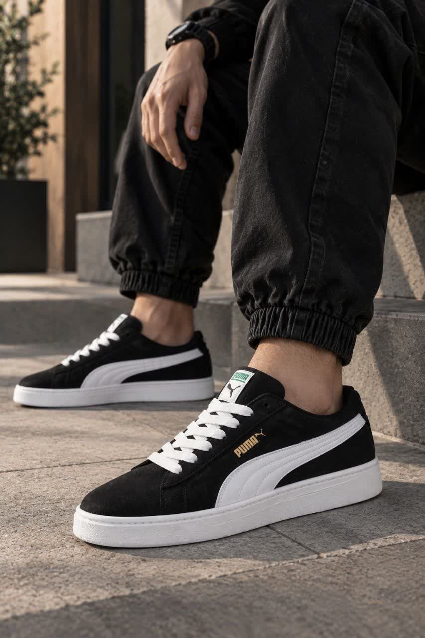 کتانی اسپرت پوما مشکی با خط سفید و لوگوی طلایی در کنار جعبه Puma