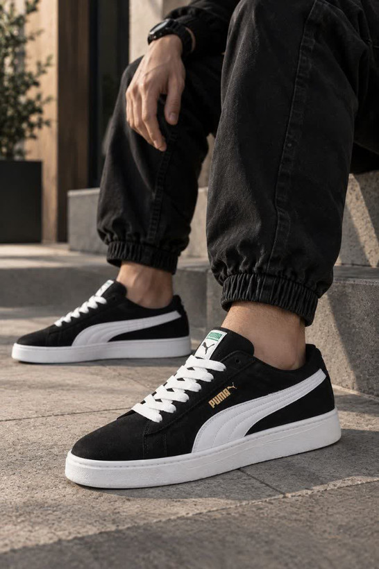 کتانی اسپرت پوما مشکی با خط سفید و لوگوی طلایی در کنار جعبه Puma
